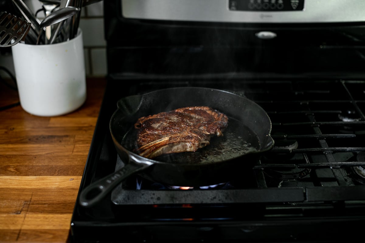 A photo of a seared steak in a cast iron skillet over high flame heat on a gas range.