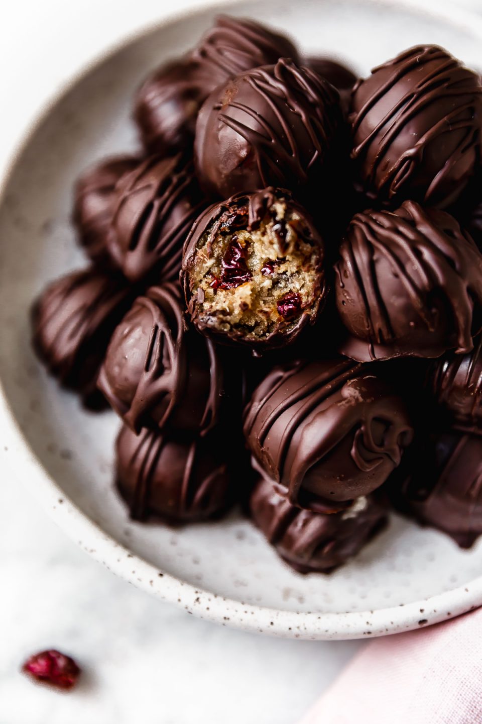 Chocolate-covered vegan cookie dough bites in a white serving bowl. One of the bites has a bite taken out of it.