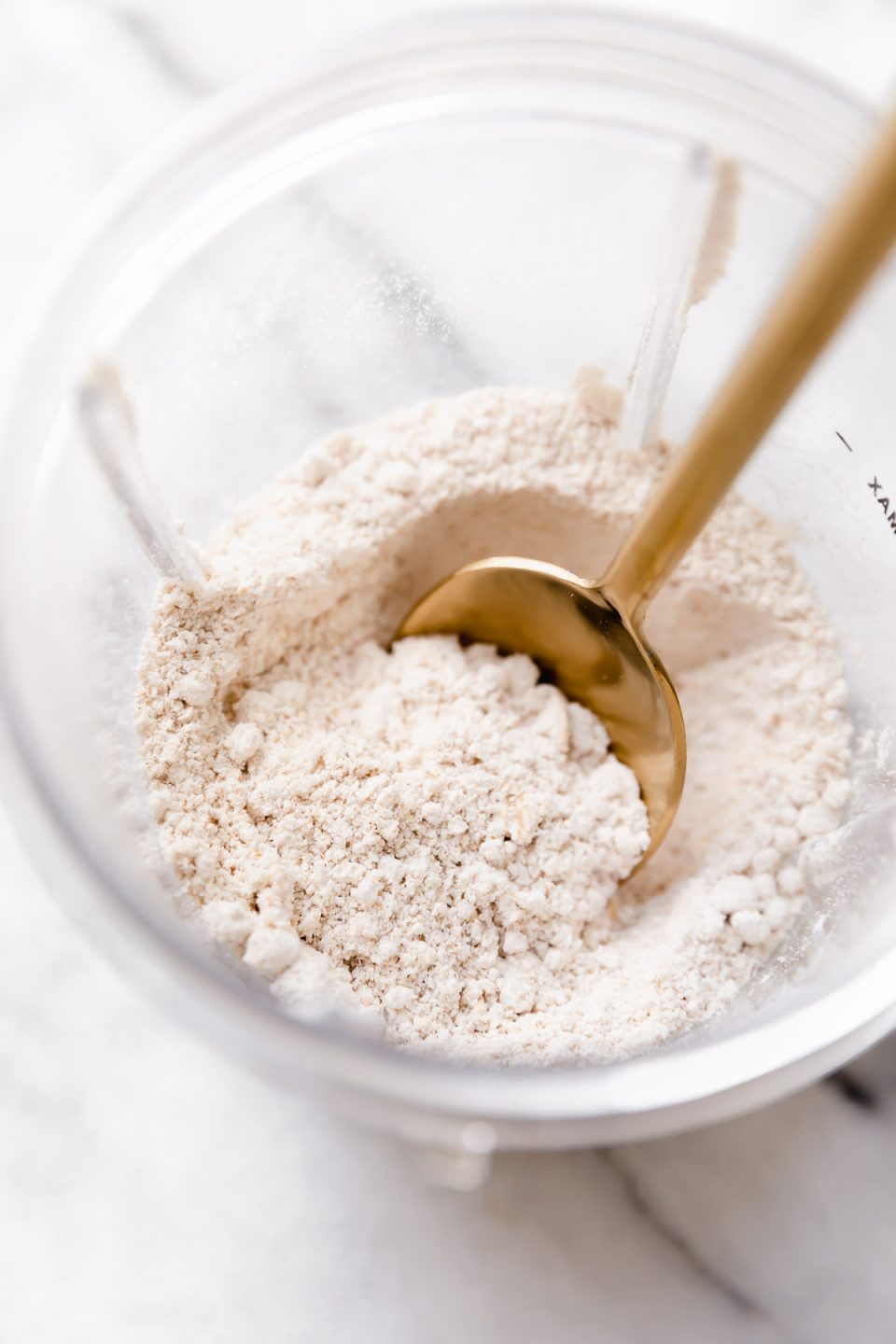 Oat flour in a blender cup with a gold spoon.