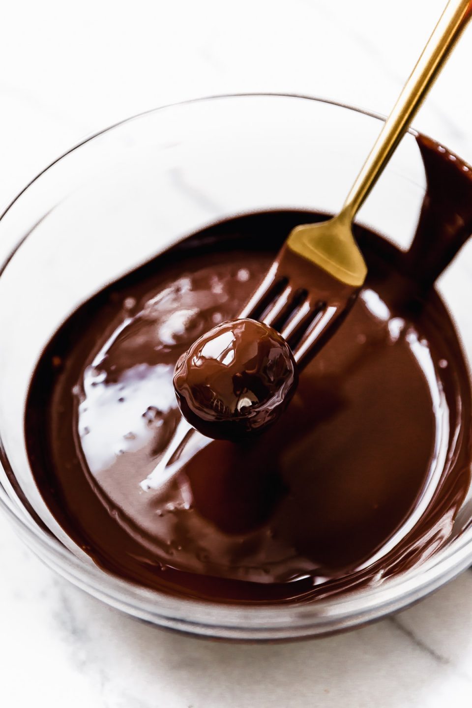 Pulling vegan cookie dough bite out of bowl of dark chocolate with a gold fork.