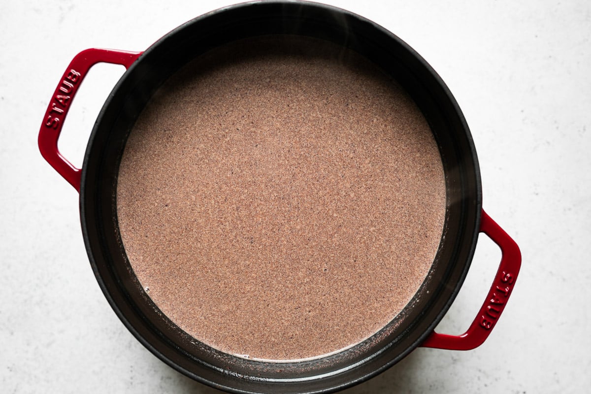 How to make homemade hot cocoa: chocolate melted (even more) into the milk mixture in a red Staub dutch oven, which sits atop a white surface.