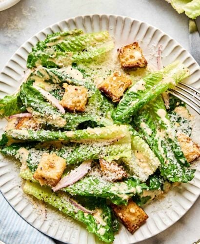 An overhead shot of Caesar salad on a white scalloped plate atop a white marbled surface.