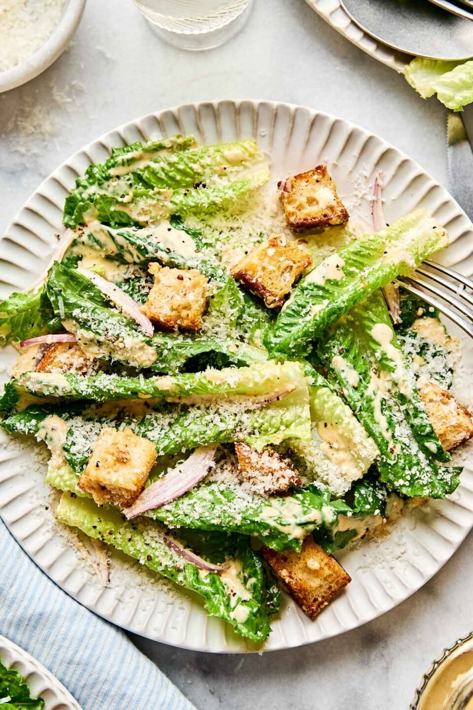 An overhead shot of Caesar salad on a white scalloped plate atop a white marbled surface.