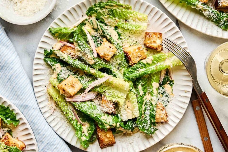 An overhead shot of a Caesar side salad on a white scalloped plate atop a white marbled surface.