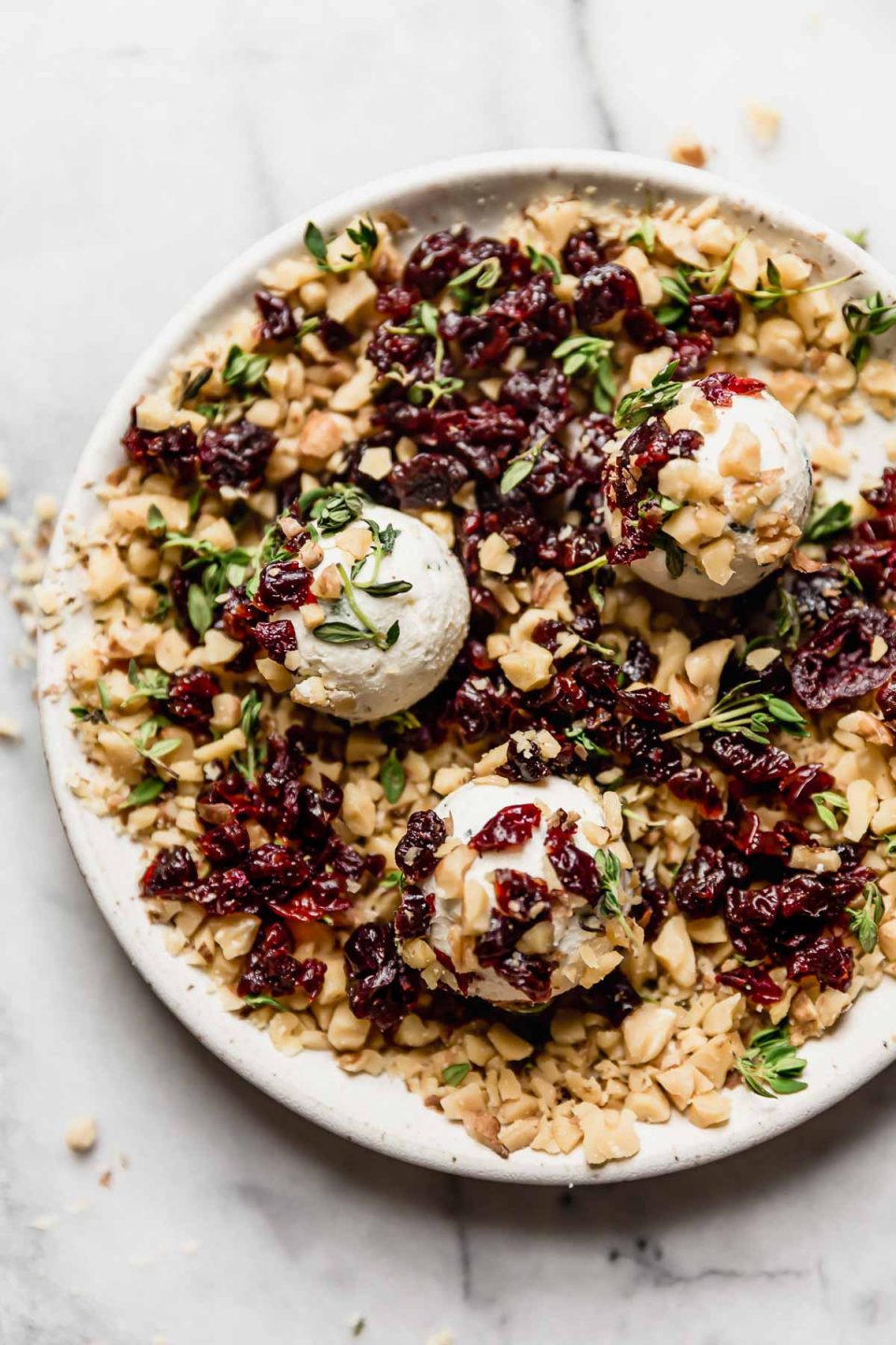 Rolling goat cheese balls in coating of chopped nuts & dried Montmorency tart cherries on a small white plate.