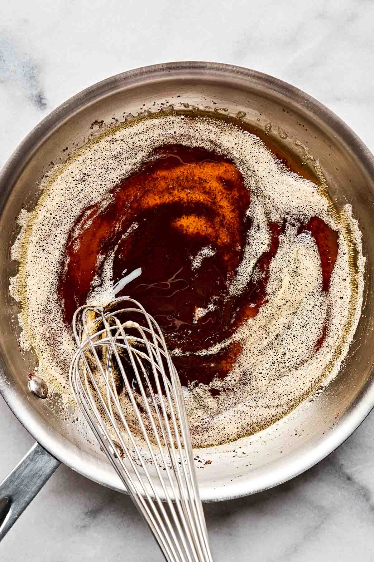 An overhead shot of browned butter being whisked in a skillet atop a white marbled surface.
