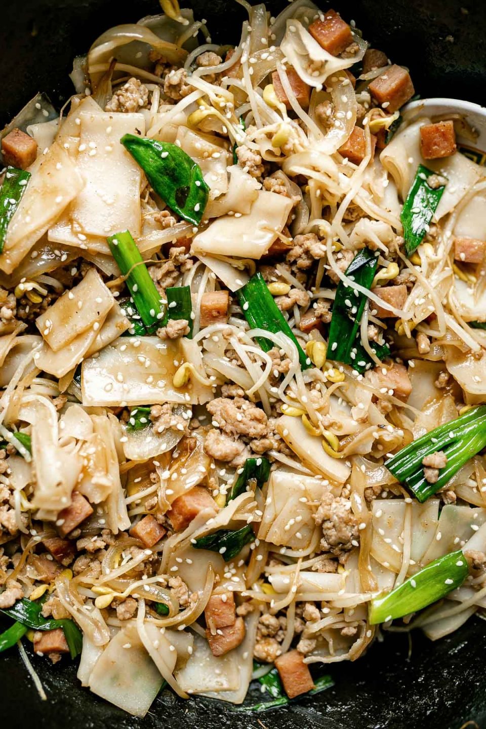 Close up of Hawaiian-style pork chow fun in a Staub cast iron wok. The chow fun is garnished with sesame seeds.