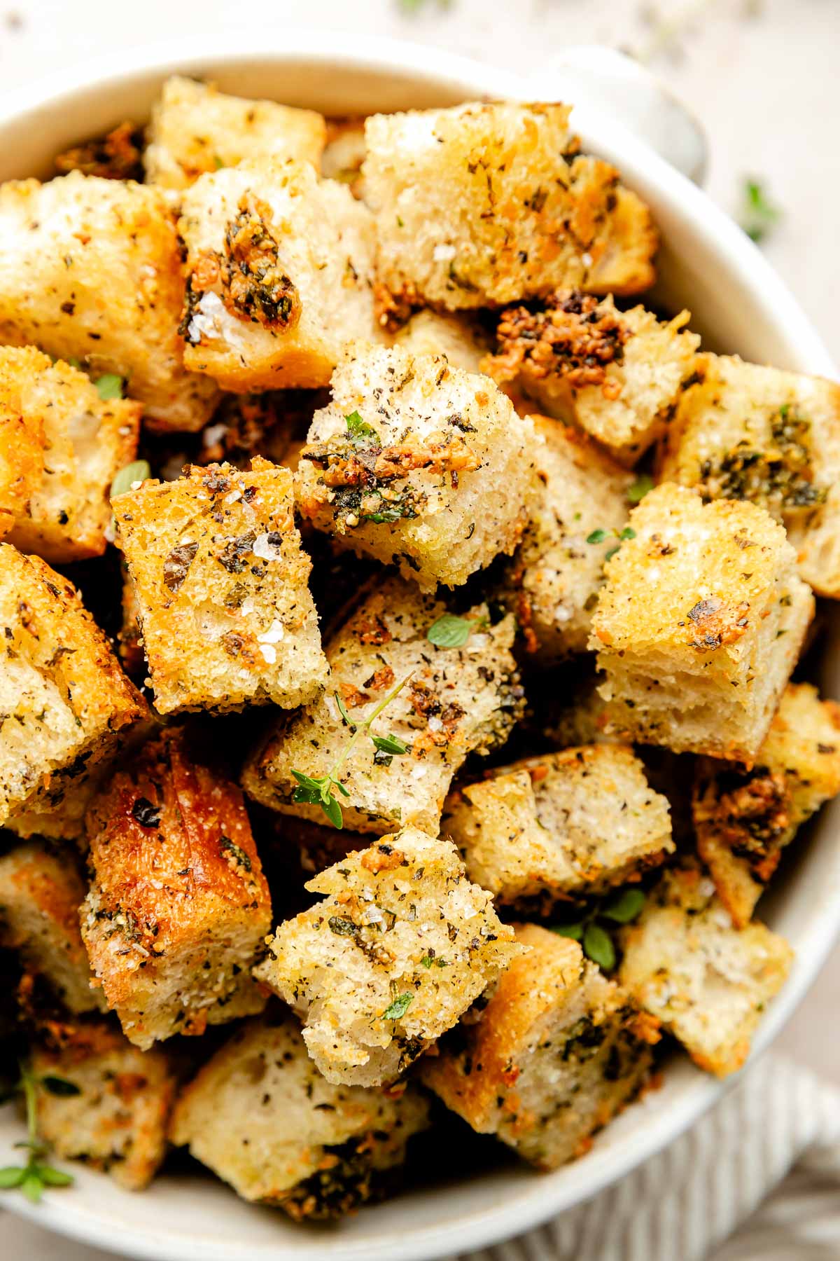 An close-up overhead shot of homemade croutons garnished with fresh herbs and sea salt in a white bowl.
