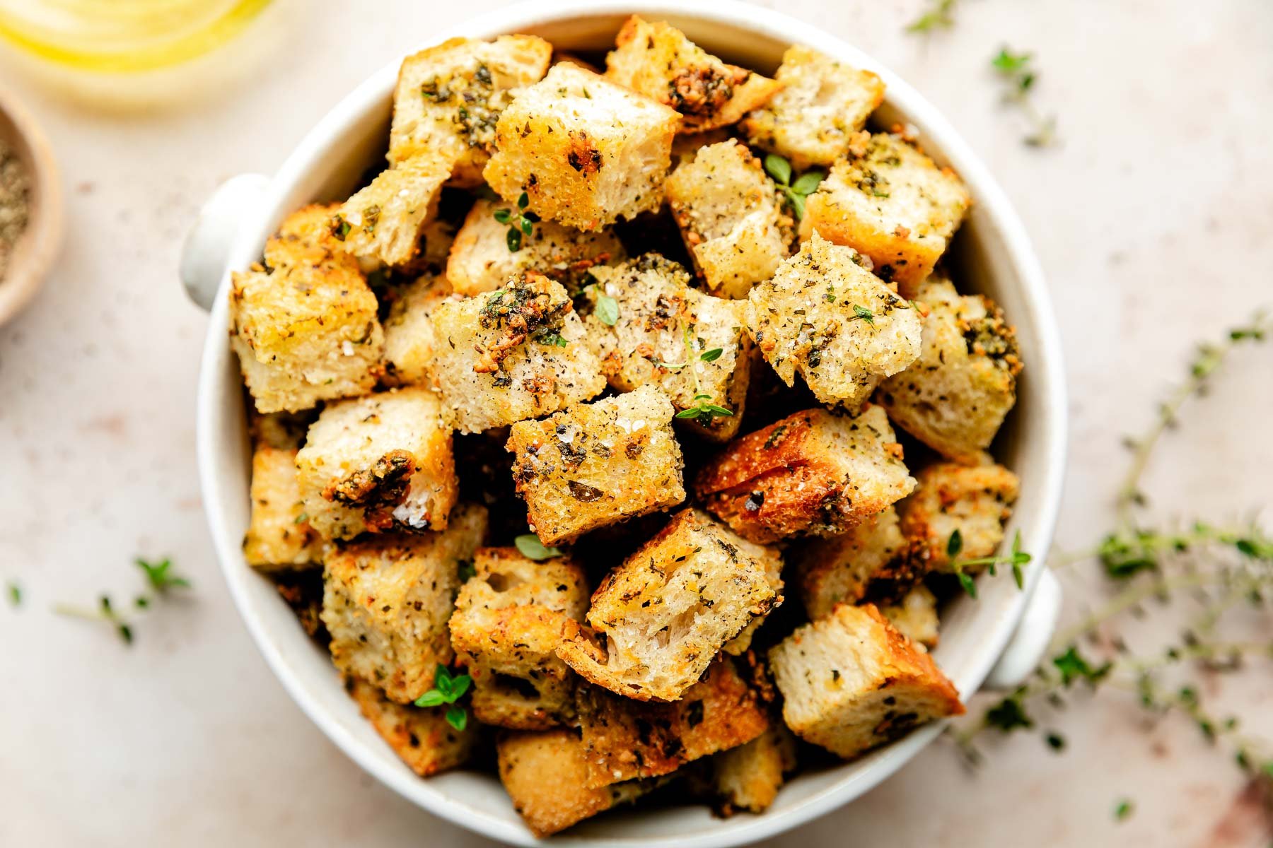 An close-up overhead shot of homemade croutons in a white bowl atop an off-white surface.