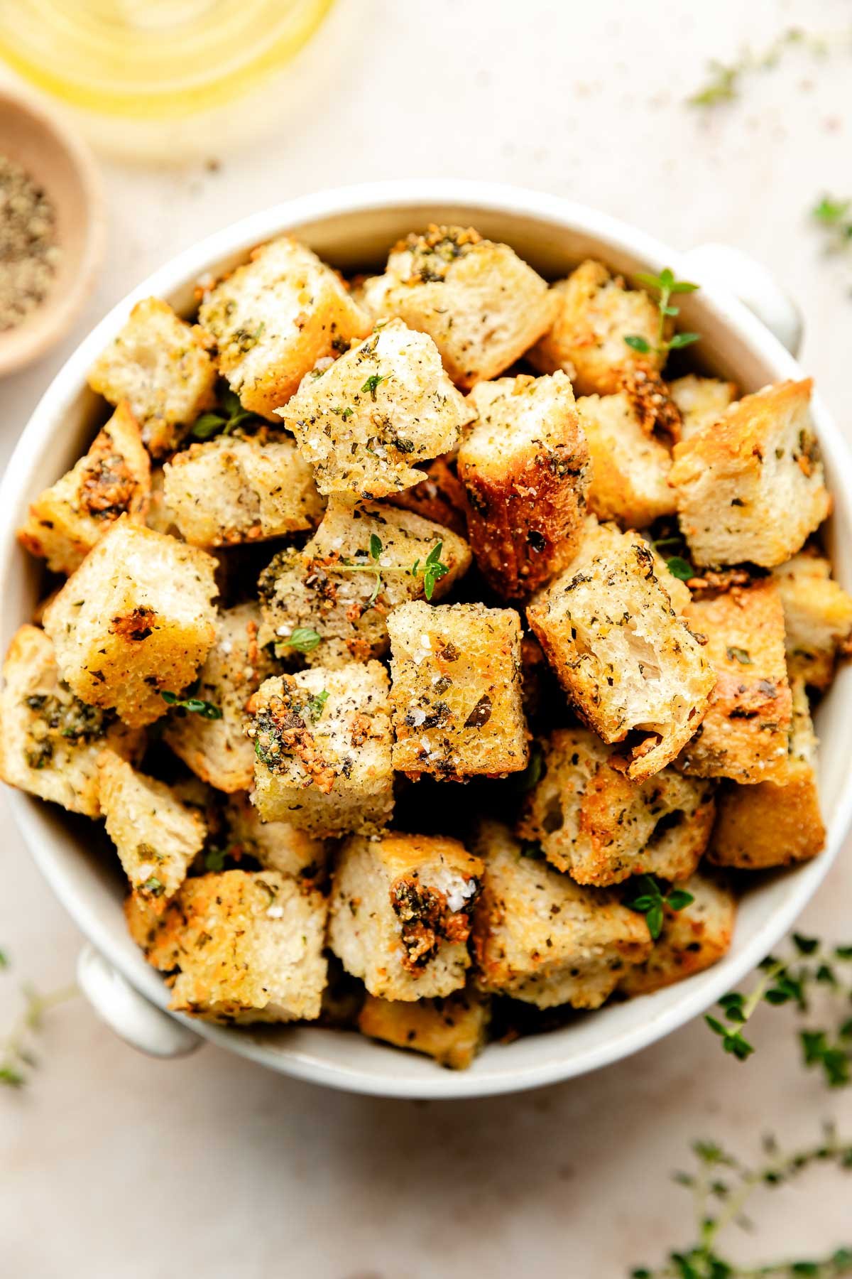 An close-up overhead shot of homemade croutons in a white bowl atop an off-white surface.