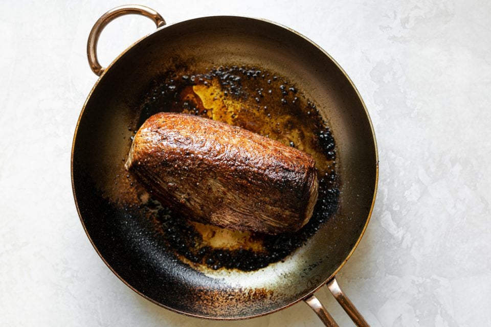 Seared beef tenderloin, in a large skillet atop a white surface.