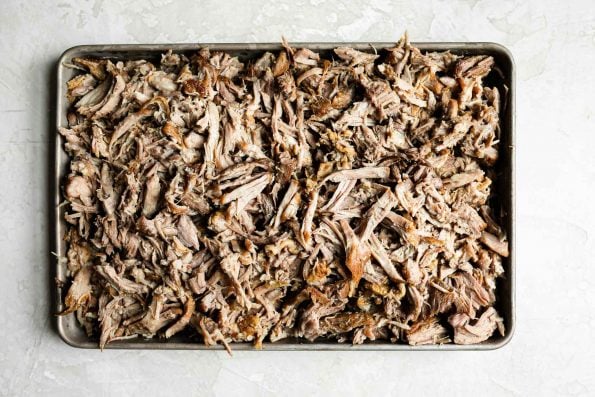 Shredded kalua pork on a small baking sheet sitting atop a creamy cement backdrop.