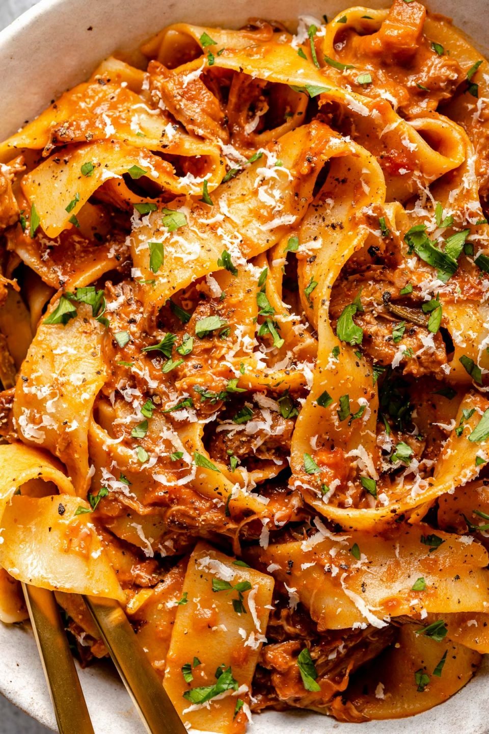 Close up of lamb ragu pappardelle, topped with freshly grated parmesan and chopped parsley.