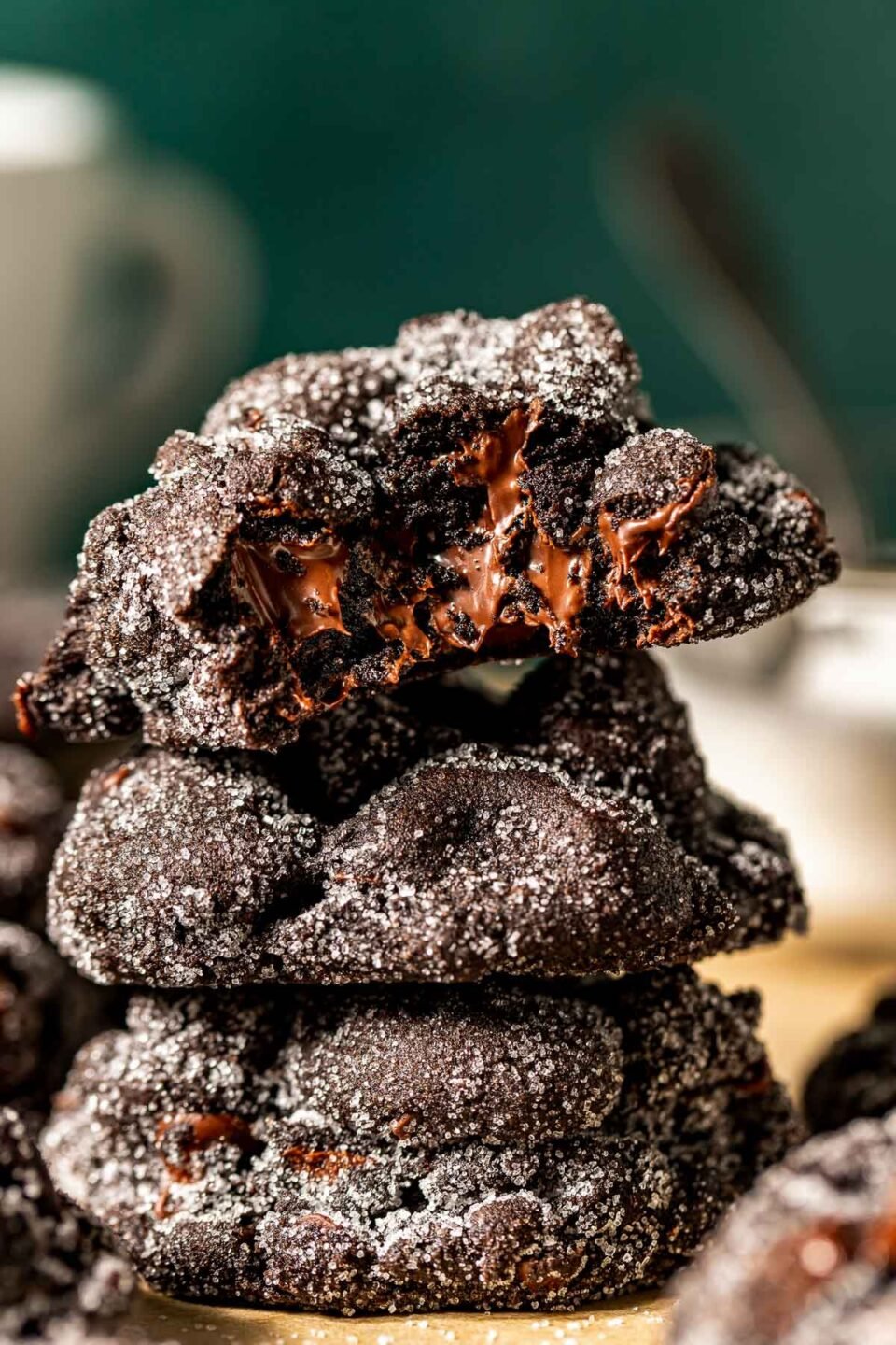 A side shot of three stacked bittersweet chocolate cookies on a sheet of parchment paper. The top cookie has a bite taken out of it, displaying gooey chocolate chips.