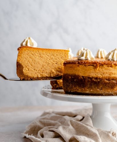 Pulling a slice of pumpkin cheesecake out of the cheesecake with a cake server.