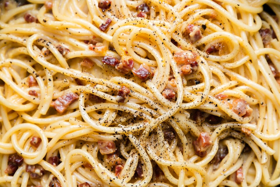 A close up shot of finished pasta carbonara garnished with ground black pepper.