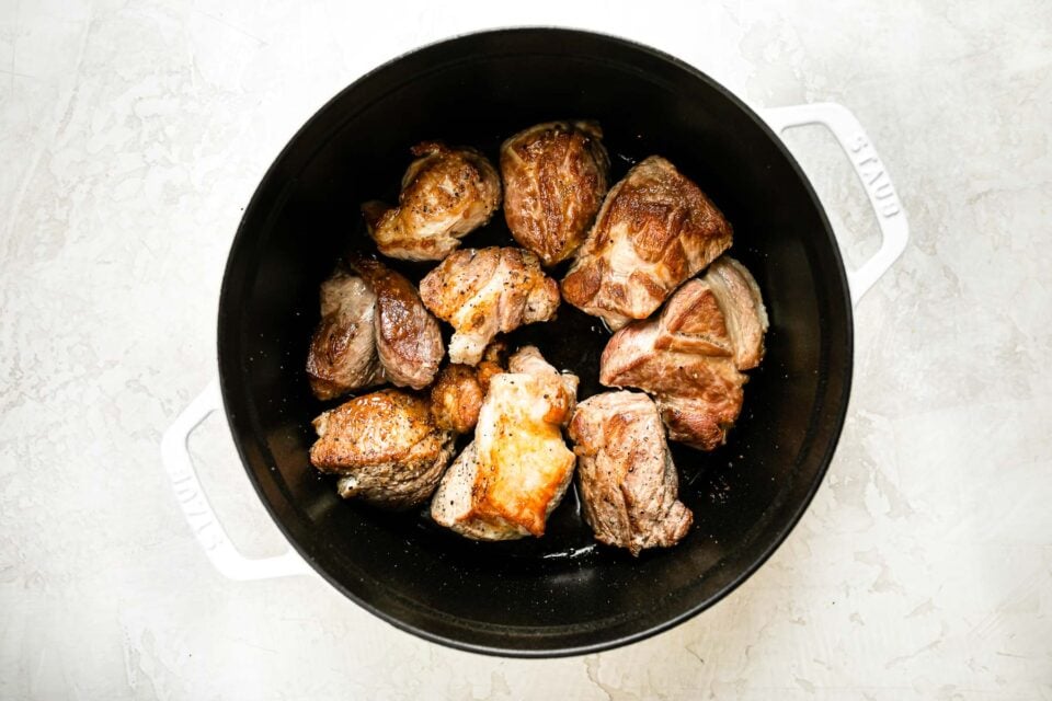 Browned pork shoulder in a large white Dutch oven.