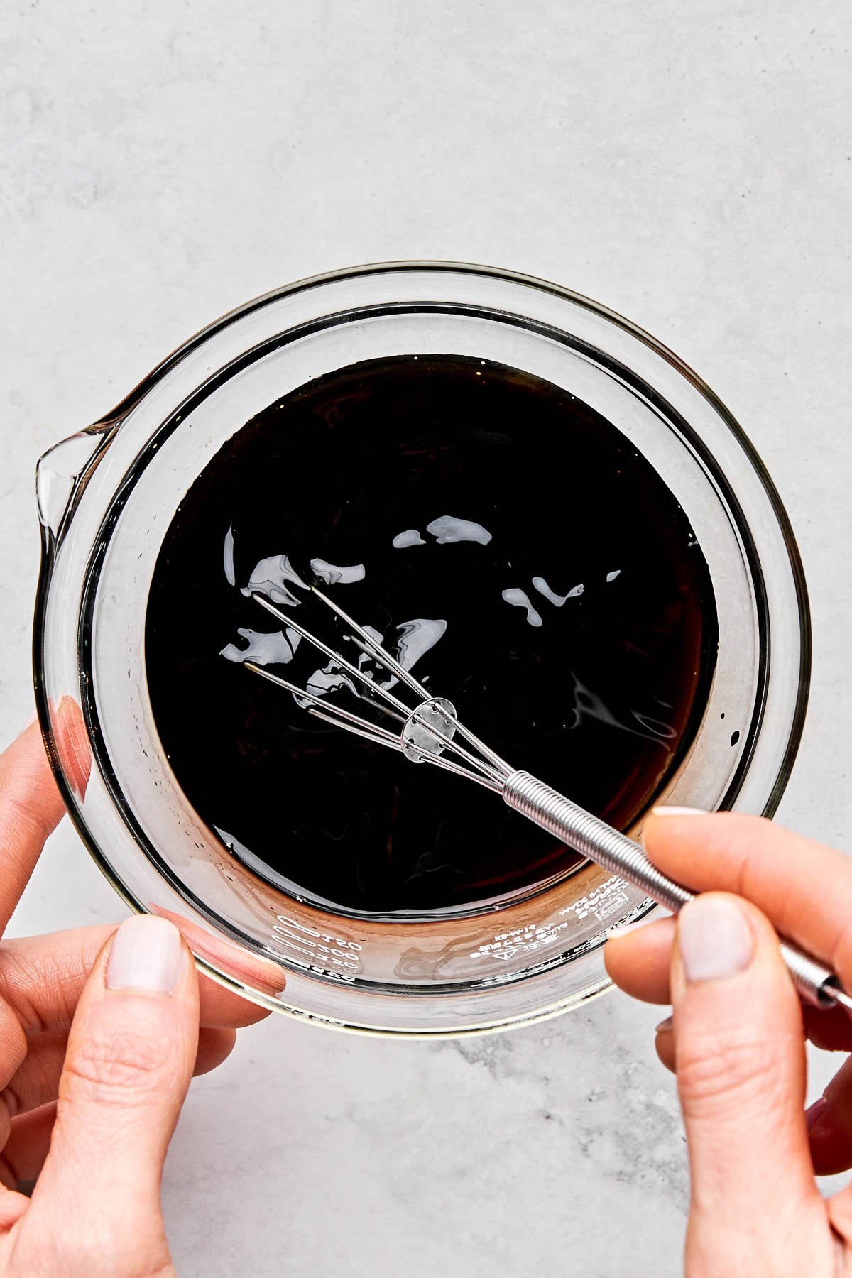 An overhead shot of stir fried vegetable noodles on a white stoneware plate on a white marbled surface. The plate is surrounded by a wok of noodles and a small blue dish of sliced green onions.