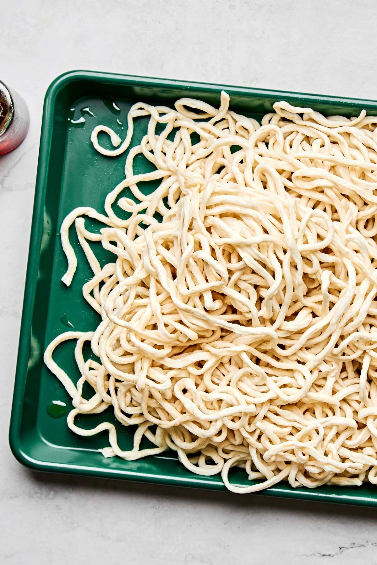 An overhead shot of a woman's hands holding and whisking stir fry sauce in a liquid glass measuring cup over a white marbled surface.